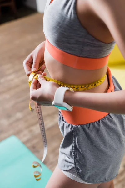 Cropped view of sportswoman measuring waist with tape at home — Stock Photo