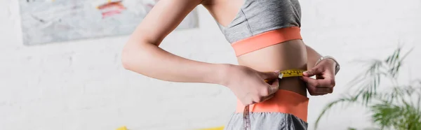 Orientación panorámica de la deportista midiendo cintura con cinta adhesiva en casa - foto de stock