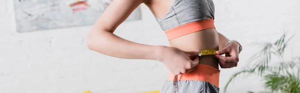 Panoramic orientation of sportswoman measuring waist with tape at home — Stock Photo