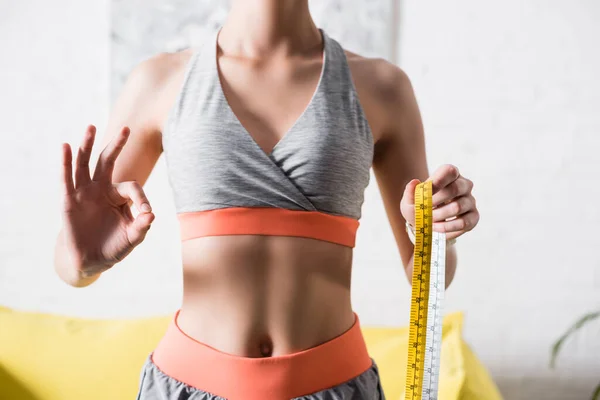 Cropped view of sportswoman showing okay gesture and holding measuring tape — Stock Photo