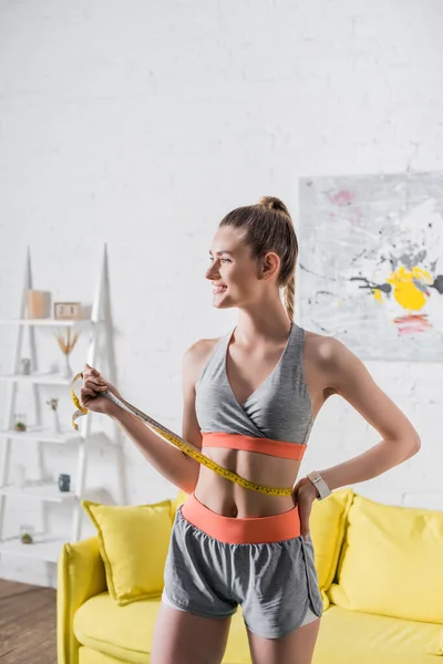 Frontansicht einer Sportlerin mit Maßband über der Taille, die zu Hause wegschaut — Stockfoto