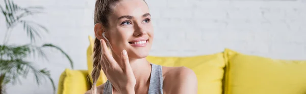 Panoramic shot of young adult woman with wireless earphone at home — Stock Photo