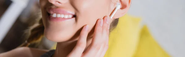 Panoramic shot of young woman touching wireless earphone — Stock Photo