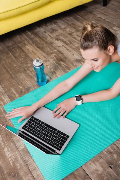 Esportista sorrindo usando laptop no tapete de fitness em casa — Fotografia de Stock