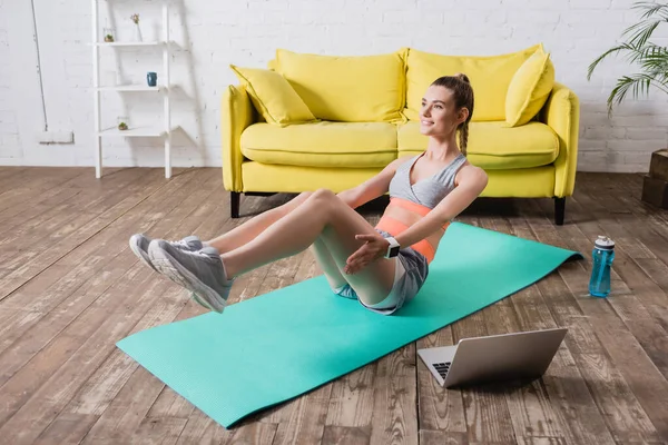 Positive Sportlerin trainiert neben Laptop und Wasserflasche am Boden — Stockfoto