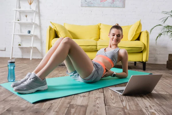 Молодая женщина в спортивной одежде смотрит на ноутбук во время тренировки дома — стоковое фото