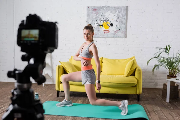 Focus selettivo della sportiva che si esercita sul tappeto fitness vicino alla fotocamera digitale a casa — Foto stock