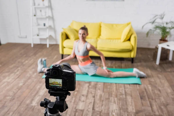 Selektiver Fokus der Frau in Sportbekleidung beim Split auf Fitnessmatte in der Nähe der Digitalkamera — Stockfoto