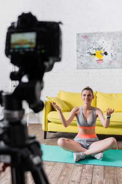 Selektiver Fokus einer lächelnden Sportlerin, die zu Hause auf der Fitnessmatte in die Digitalkamera lächelt — Stockfoto