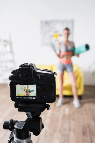 Enfoque selectivo de la cámara digital cerca de la deportista con botella deportiva y colchoneta de fitness en casa — Stock Photo