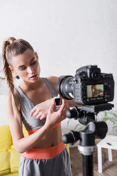 Foco seletivo da esportista mostrando relógio inteligente na câmera digital em casa — Fotografia de Stock