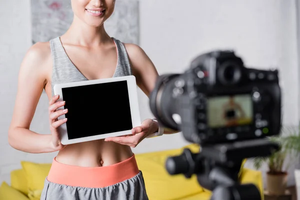 Cropped view of sportswoman holding digital tablet near digital camera at home — Stock Photo