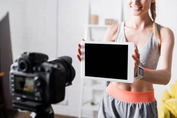 Обрезанный вид веселой спортсменки, показывающей цифровой планшет с чистым экраном на цифровую камеру — стоковое фото