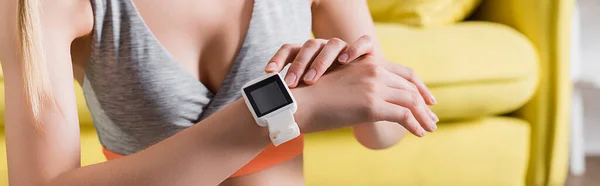 Panoramic crop of sportswoman touching smartwatch at home — Stock Photo