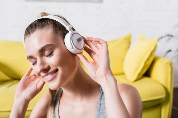 Mujer sonriente con los ojos cerrados escuchando música en los auriculares en casa - foto de stock