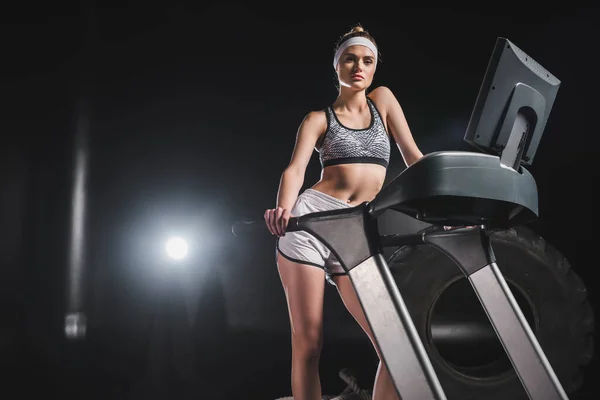 Deportiva mirando la cámara mientras está de pie en la cinta de correr en el gimnasio - foto de stock