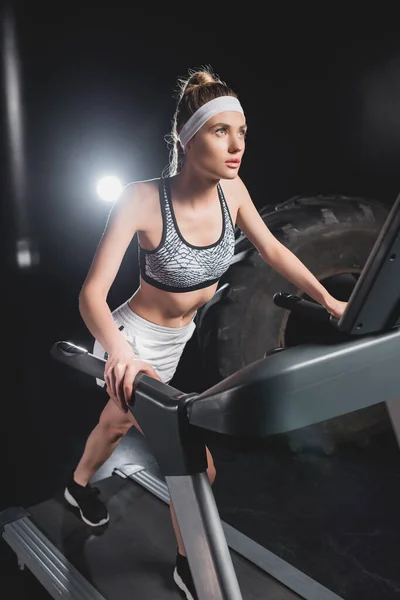 Selective focus of young sportswoman running on treadmill near tire in sports center — Stock Photo