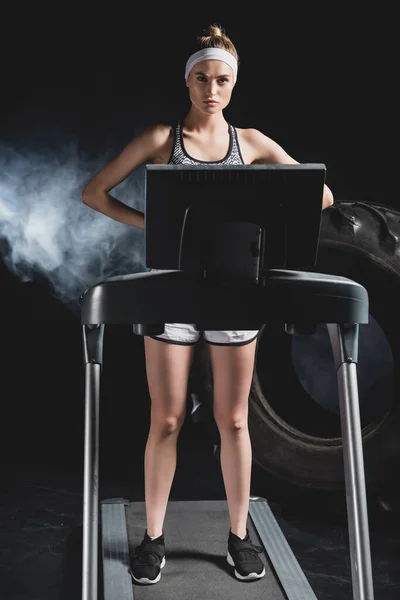 Young sportswoman standing on treadmill near tire in sports center with smoke — Stock Photo