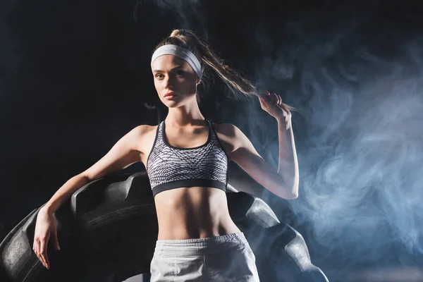 Concentration sélective des sportives touchant les cheveux près du pneu dans le centre sportif avec de la fumée — Photo de stock