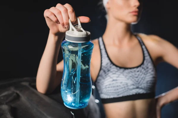 Selective focus of sportswoman holding sports bottle near tire in gym — Stock Photo