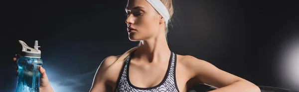 Panoramic orientation of sportswoman holding sports bottle in gym with smoke — Stock Photo