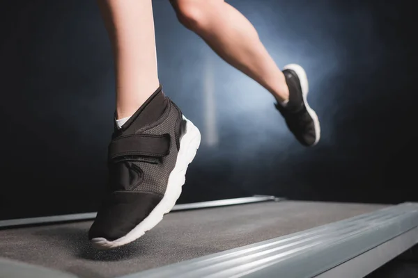 Cropped view of sportswoman in sneakers training on treadmill in gym with smoke — Stock Photo