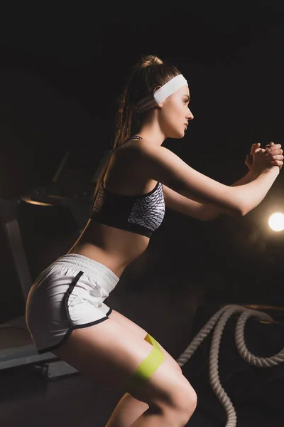 Vista lateral del entrenamiento de la joven deportista con banda de resistencia en el gimnasio - foto de stock