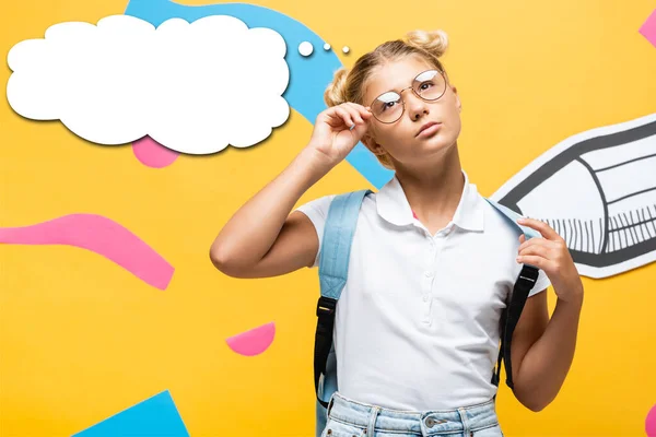 Nachdenkliches Schulmädchen berührt Brille in der Nähe von Bleistift, abstrakten Elementen und Gedankenblasenillustration auf gelb — Stockfoto