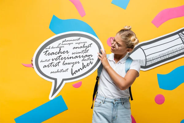 Skeptische Schülerin hält Sprechblase mit Schriftzug in der Nähe von Bleistift und abstrakten Elementen auf gelb — Stockfoto