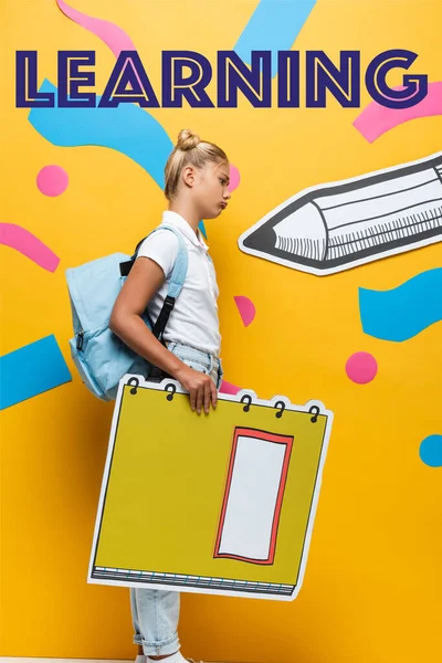 Seitenansicht eines aufgebrachten Schulmädchens mit Notizbuch-Maquette in der Nähe von Schriftzug, Bleistift und dekorativen Elementen auf gelb — Stockfoto