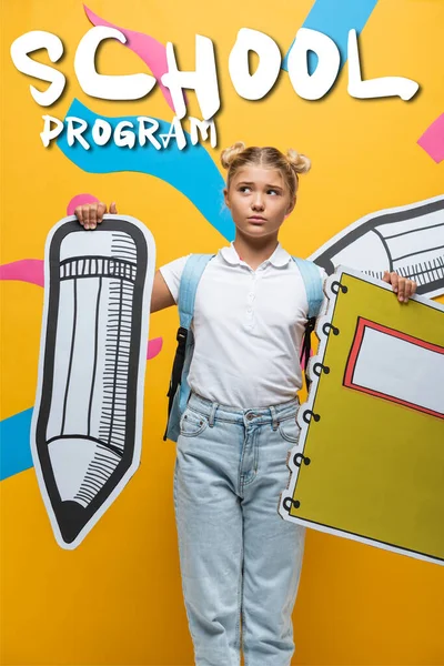 Thoughtful schoolkid holding paper pencil and notebook near school program lettering on yellow — Stock Photo