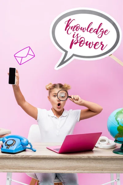 Estudante segurando lupa e smartphone com tela em branco perto da bolha de fala com conhecimento é poder lettering, globo e laptop em rosa — Fotografia de Stock