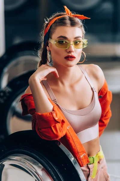 Selektiver Fokus der trendigen Frau mit Sonnenbrille, die in die Kamera neben der Waschmaschine blickt — Stockfoto