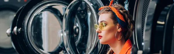 Femme élégante dans les lunettes de soleil près des machines à laver dans la laverie automatique, bannière — Photo de stock