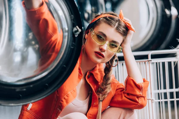 Young woman in sunglasses sitting washing machines with blurred foreground — Stock Photo