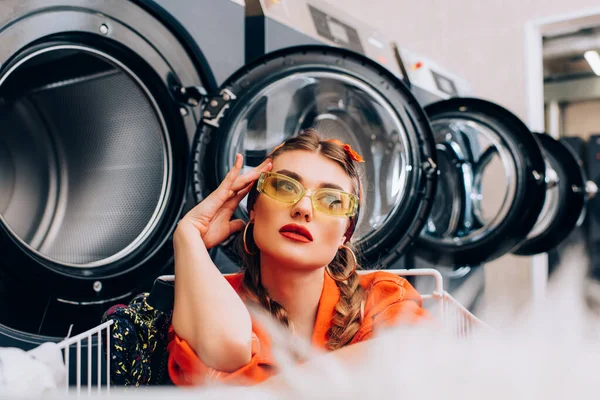 Mulher pensativa perto de máquinas de lavar roupa com primeiro plano borrado — Fotografia de Stock