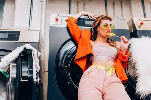 Femme à la mode dans les lunettes de soleil mordant sucette dans la laverie automatique moderne — Photo de stock