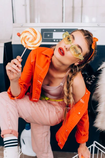 Fashionable woman holding sweet lollipop in laundromat — Stock Photo