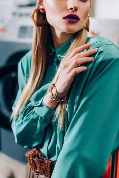 Cropped view of stylish woman touching blue blouse in public laundromat — Stock Photo