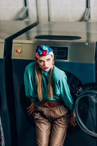 Jeune femme en turban debout près de la machine à laver dans la laverie automatique — Photo de stock