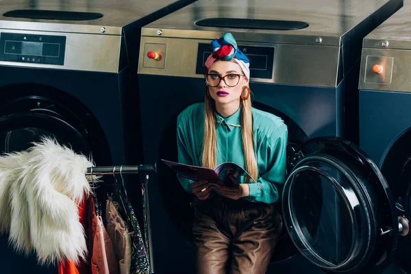 Стильная женщина в тюрбане и очки холдинг журнал в прачечной — стоковое фото