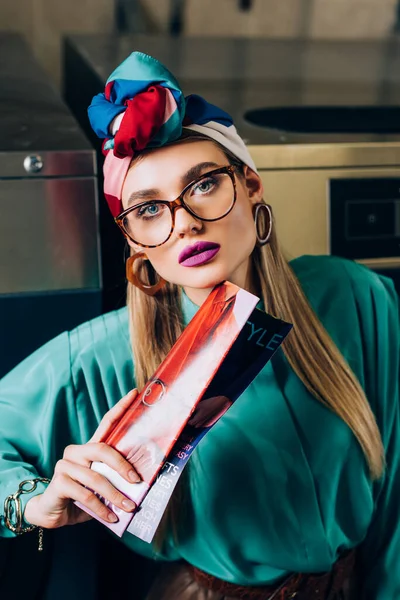 Mulher em óculos e turbante segurando revista na lavanderia pública — Fotografia de Stock