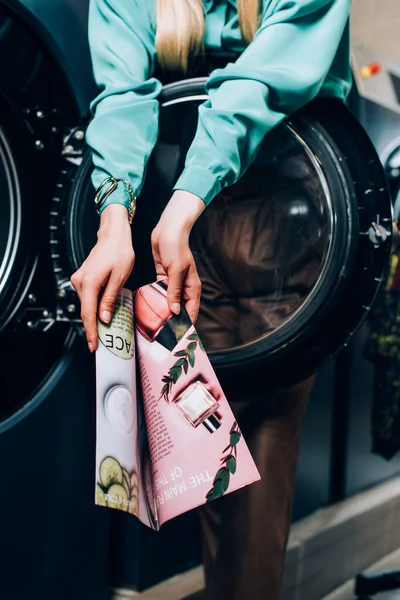 Cropped view of young woman holding magazine in public laundromat — Stock Photo