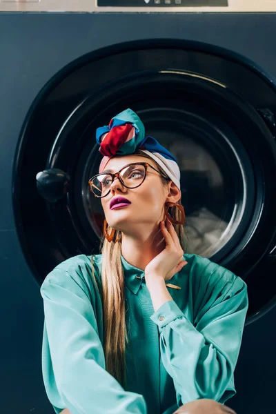 Stylish young woman in glasses and turban in laundromat — Stock Photo