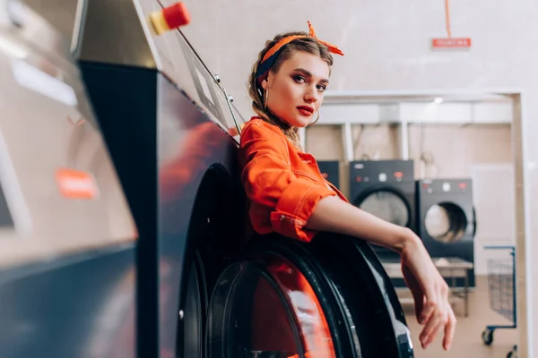 Стильна жінка в обкладинці, дивлячись на камеру в сучасному пральні — стокове фото