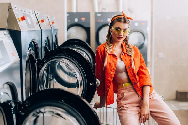 Trendy woman in headband and sunglasses in modern laundromat — Stock Photo