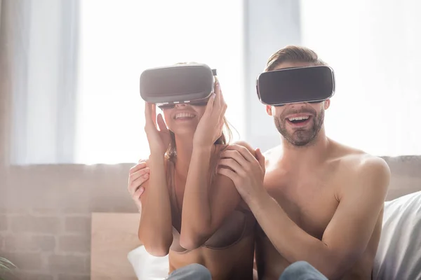 Fröhlicher Mann berührt lächelnde Freundin, während er VR-Headsets im Schlafzimmer benutzt — Stockfoto
