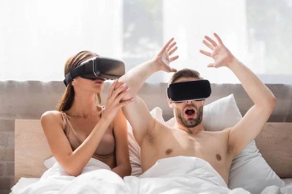 Young woman touching scared boyfriend using vr headset in bedroom — Stock Photo