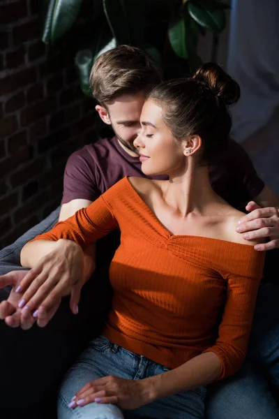 Junger Mann umarmt Freundin, während er zu Hause sitzt — Stockfoto