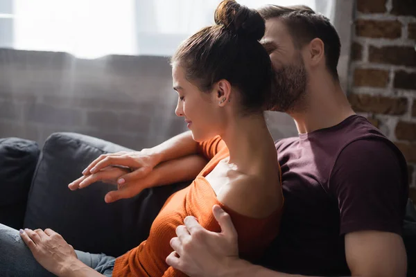 Tender man embracing beloved woman while sitting on sofa at home — Stock Photo